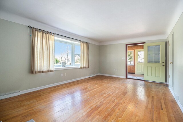 empty room with baseboards, baseboard heating, light wood finished floors, and visible vents
