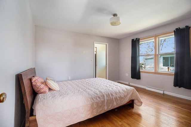 bedroom with baseboards, a baseboard radiator, and wood-type flooring