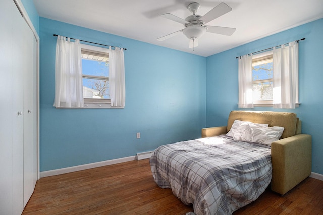 bedroom featuring a ceiling fan, baseboards, wood finished floors, a baseboard radiator, and a closet