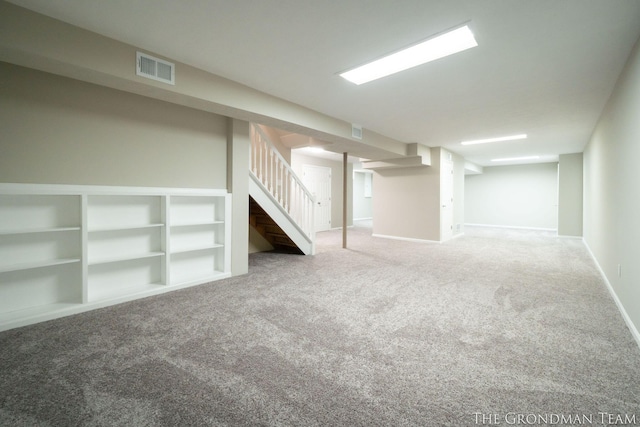 finished below grade area featuring carpet floors, baseboards, visible vents, and stairway