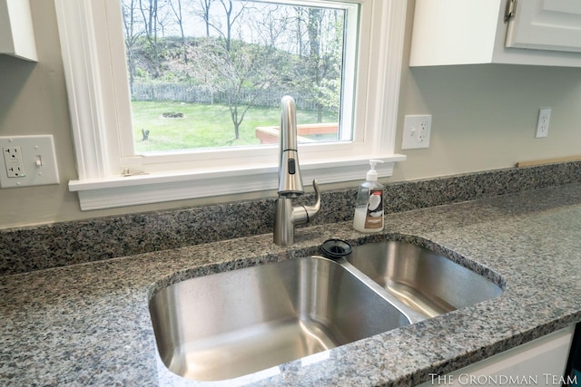 details featuring a sink, white cabinets, and dark stone countertops