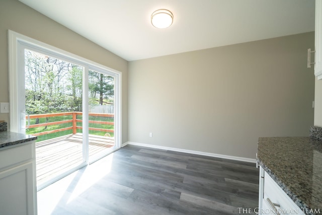 unfurnished dining area featuring baseboards and dark wood-style flooring