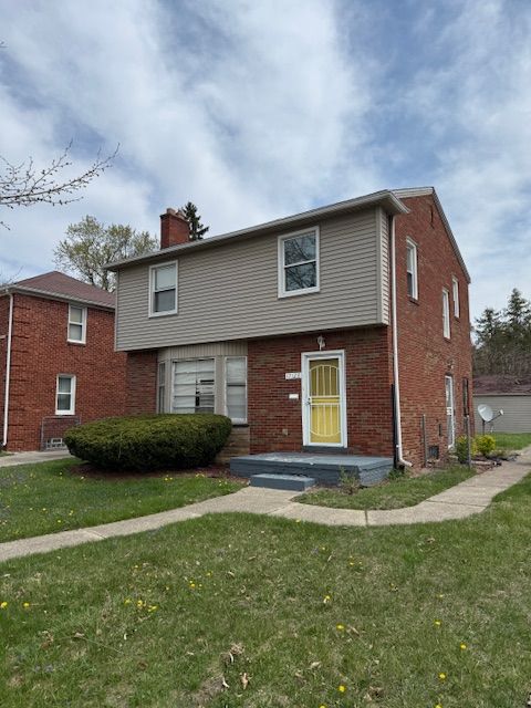 view of front of home with a chimney, brick siding, and a front yard