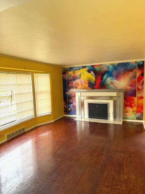 unfurnished living room featuring a fireplace with flush hearth, baseboards, wood finished floors, and visible vents