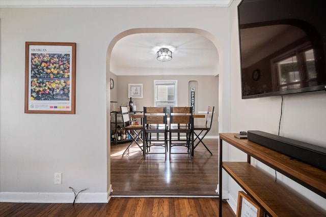 dining space featuring arched walkways, baseboards, and wood finished floors