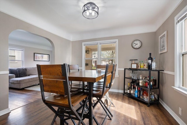 dining room with arched walkways, a dry bar, a healthy amount of sunlight, and wood finished floors