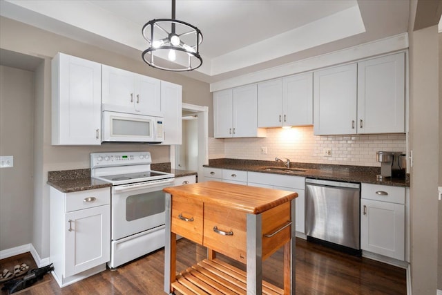 kitchen featuring dark wood-style flooring, a sink, a raised ceiling, white appliances, and tasteful backsplash