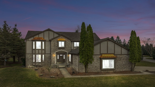tudor-style house with roof with shingles, a front yard, and stucco siding