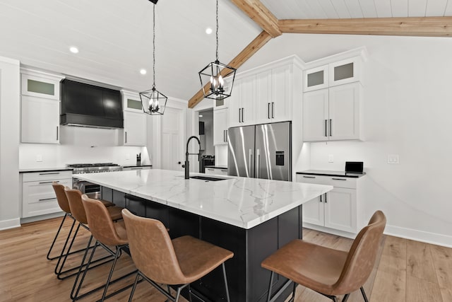 kitchen featuring appliances with stainless steel finishes, a sink, premium range hood, a center island with sink, and light wood-style floors