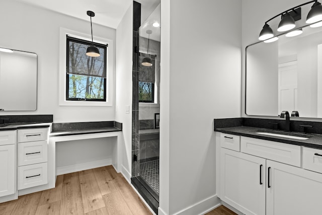 bathroom with a shower stall, two vanities, baseboards, and wood finished floors