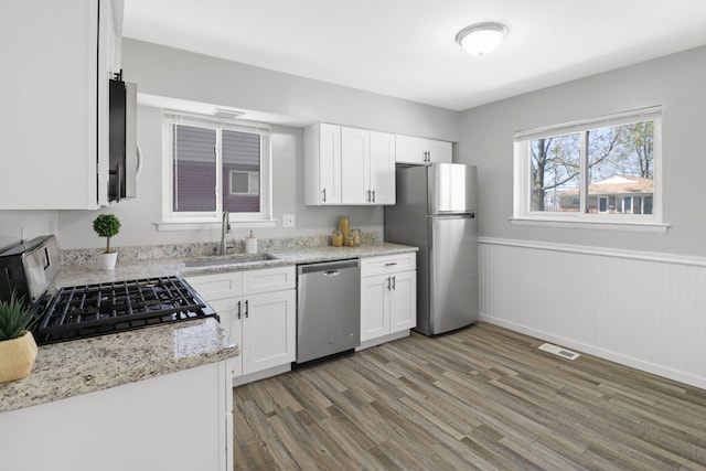 kitchen featuring appliances with stainless steel finishes, a sink, light wood-style flooring, a wainscoted wall, and visible vents