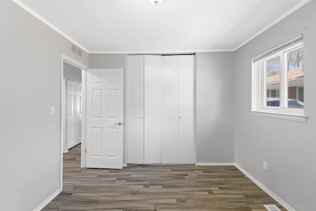unfurnished bedroom with visible vents, ornamental molding, baseboards, and wood finished floors