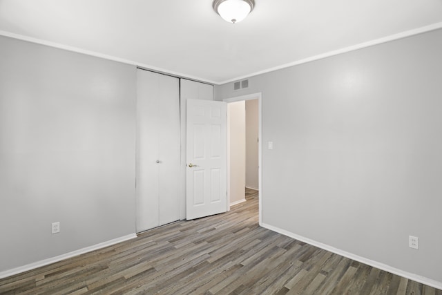 unfurnished bedroom with baseboards, visible vents, wood finished floors, and a closet