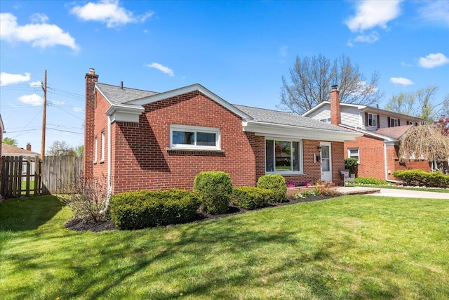 view of front of home featuring brick siding, fence, a front yard, and a chimney