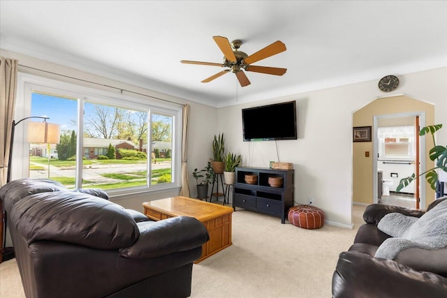 living room featuring arched walkways, baseboards, light carpet, and a ceiling fan