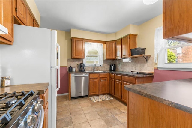 kitchen with a healthy amount of sunlight, dark countertops, tasteful backsplash, a sink, and appliances with stainless steel finishes