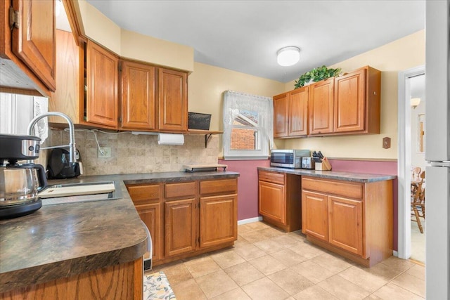 kitchen featuring dark countertops, tasteful backsplash, brown cabinets, stainless steel microwave, and light tile patterned flooring