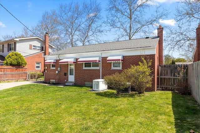 rear view of property with fence, a chimney, brick siding, entry steps, and a yard