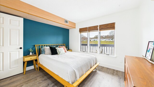 bedroom featuring a water view, baseboards, visible vents, and wood finished floors