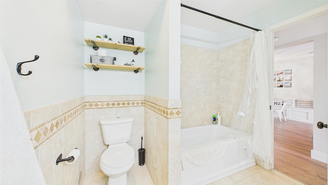 bathroom featuring wainscoting, shower / tub combo with curtain, toilet, tile patterned floors, and tile walls