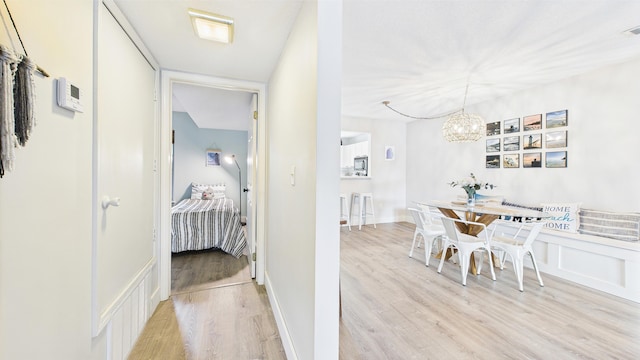 hall featuring an inviting chandelier, light wood-style flooring, a decorative wall, and wainscoting