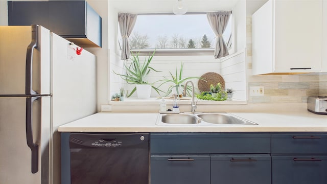 kitchen with blue cabinetry, a sink, light countertops, freestanding refrigerator, and black dishwasher