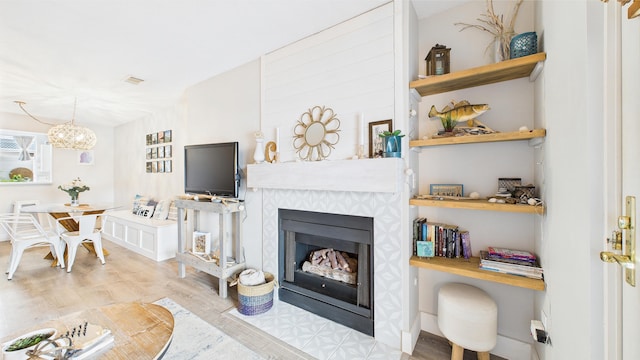 living area featuring visible vents, a fireplace with flush hearth, wood finished floors, and an inviting chandelier
