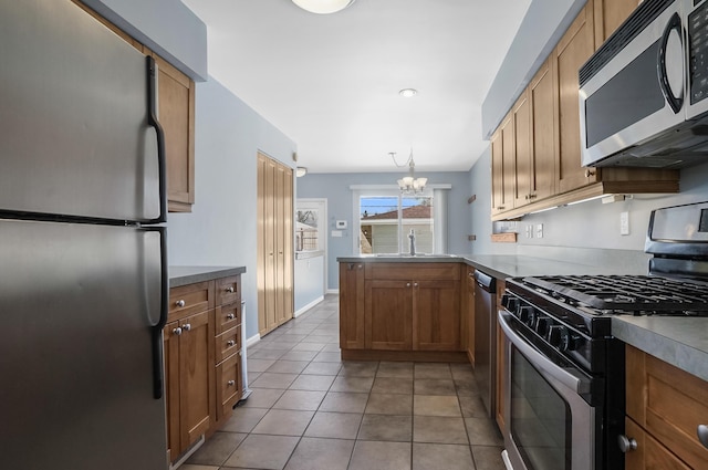 kitchen with an inviting chandelier, a sink, tile patterned floors, stainless steel appliances, and a peninsula