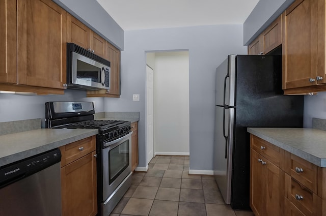 kitchen featuring dark tile patterned flooring, stainless steel appliances, and brown cabinets