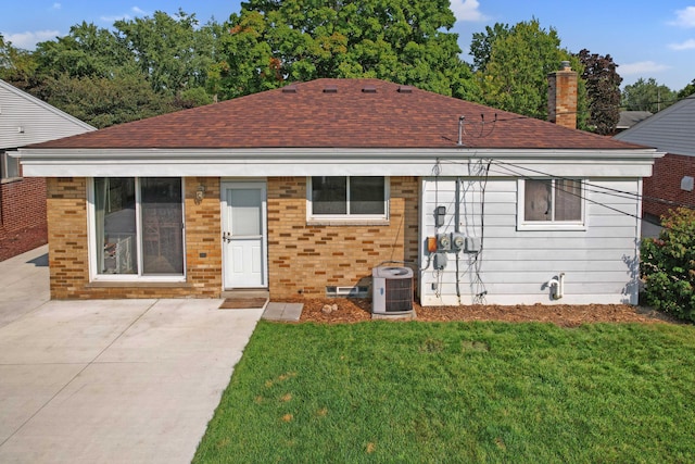 back of property featuring brick siding, central AC unit, a yard, and a shingled roof