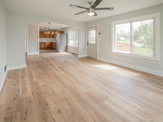 unfurnished living room featuring baseboards, arched walkways, light wood-style floors, and ceiling fan with notable chandelier