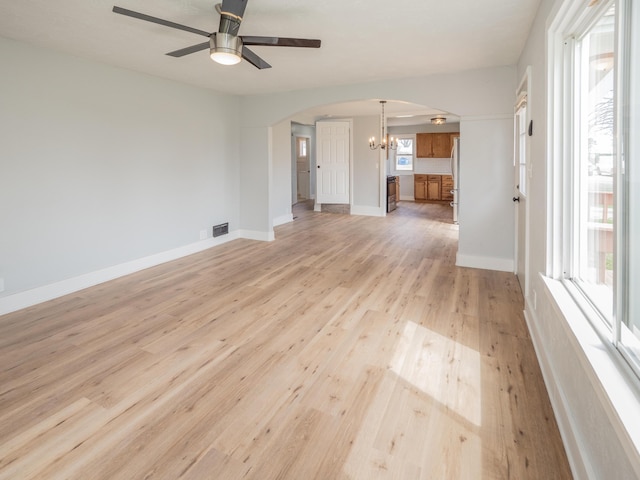 unfurnished living room featuring light wood-style floors, arched walkways, ceiling fan with notable chandelier, and visible vents