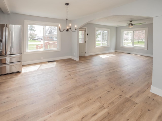 unfurnished dining area featuring baseboards, arched walkways, light wood-style flooring, and visible vents