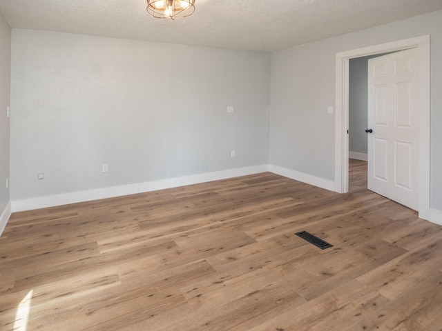 empty room with baseboards, a textured ceiling, visible vents, and wood finished floors