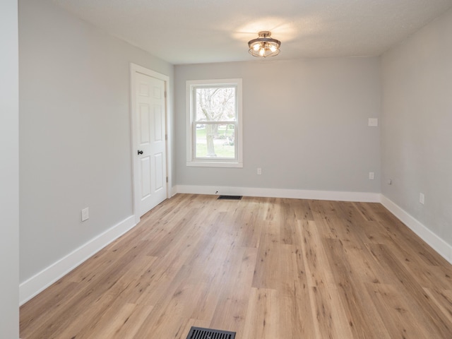 empty room with baseboards, light wood finished floors, and visible vents