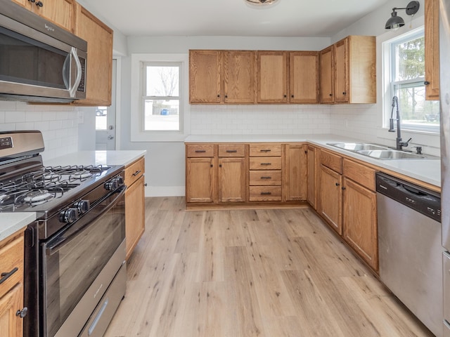 kitchen featuring decorative backsplash, appliances with stainless steel finishes, light wood-type flooring, a sink, and light countertops