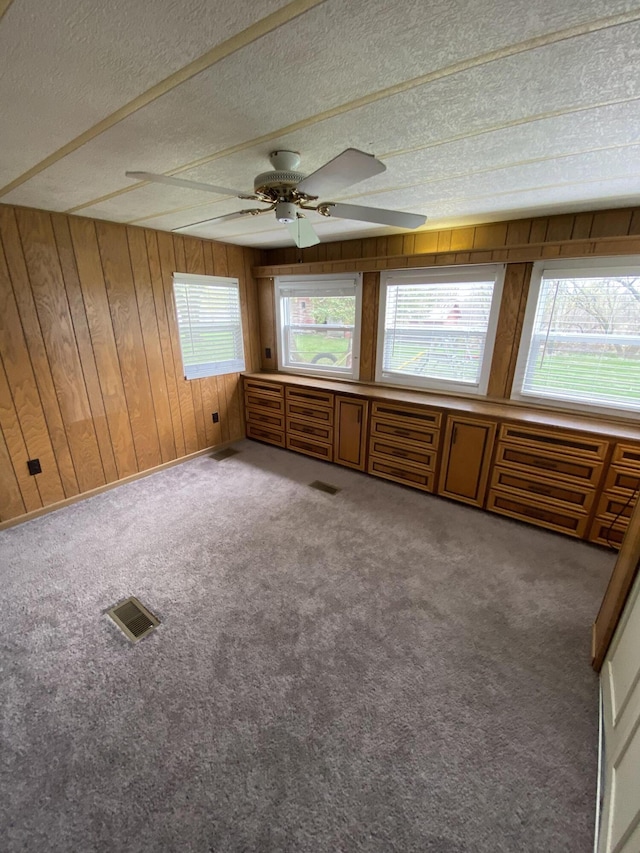 interior space featuring wooden walls, ceiling fan, a textured ceiling, and visible vents