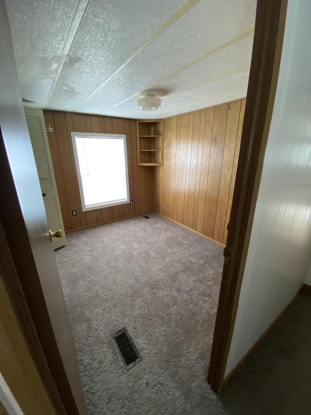 spare room with a textured ceiling, visible vents, wood walls, carpet floors, and baseboards