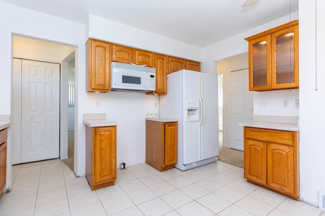 kitchen featuring light countertops, brown cabinets, white appliances, and glass insert cabinets