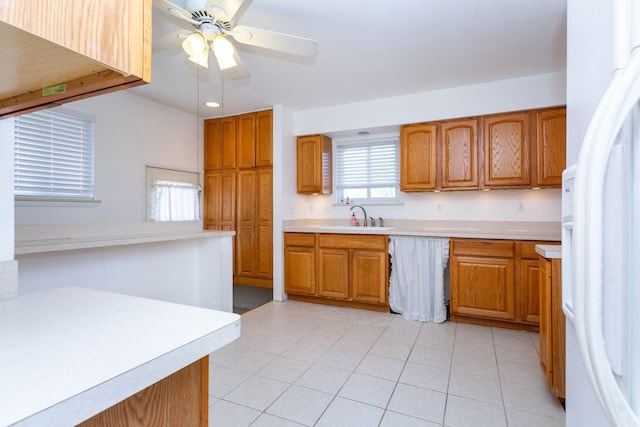 kitchen featuring ceiling fan, brown cabinets, a sink, light countertops, and freestanding refrigerator