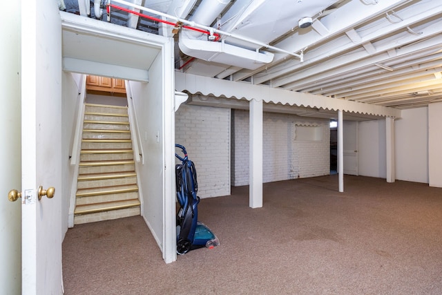 finished below grade area featuring stairs, brick wall, and carpet