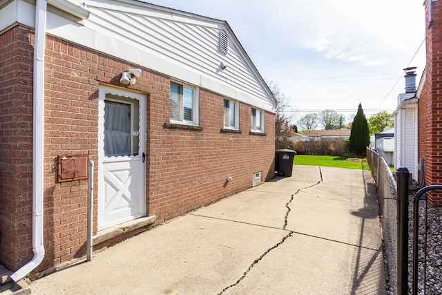 view of property exterior with fence, a patio, and brick siding