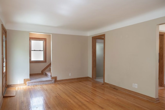 spare room with light wood finished floors, stairway, and baseboards