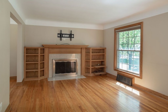 unfurnished living room with a fireplace with flush hearth, light wood finished floors, and baseboards