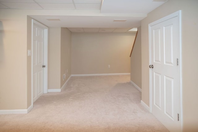 basement featuring light colored carpet, a drop ceiling, and baseboards