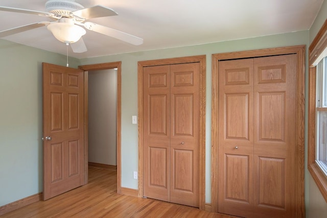 unfurnished bedroom with light wood-style flooring, two closets, baseboards, and a ceiling fan