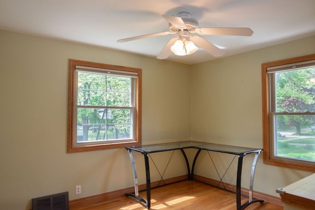 unfurnished office with plenty of natural light, wood finished floors, baseboards, and ceiling fan