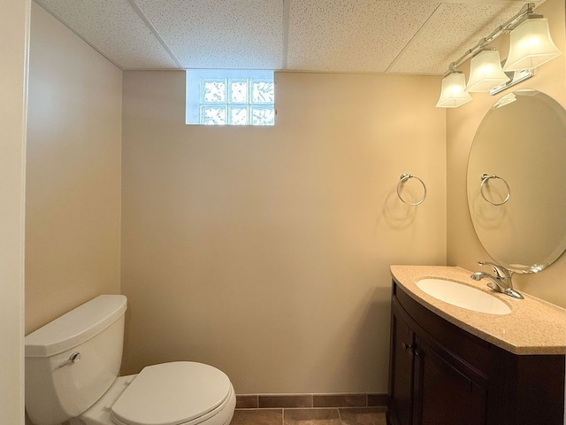 half bath with a drop ceiling, toilet, vanity, and baseboards