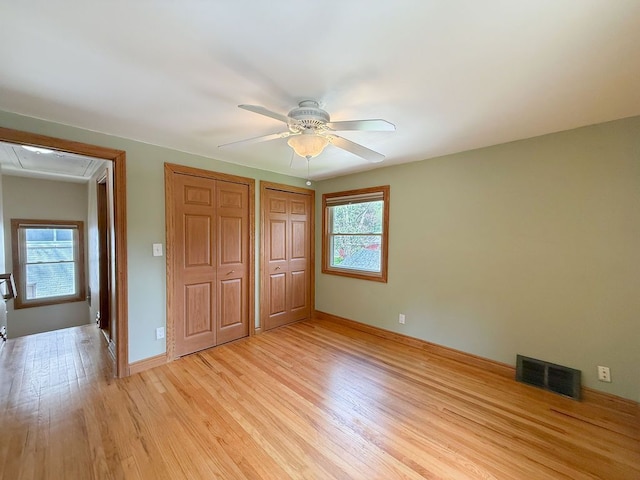unfurnished bedroom with attic access, light wood-style flooring, multiple closets, and baseboards