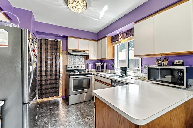 kitchen with appliances with stainless steel finishes, light countertops, a sink, a peninsula, and under cabinet range hood